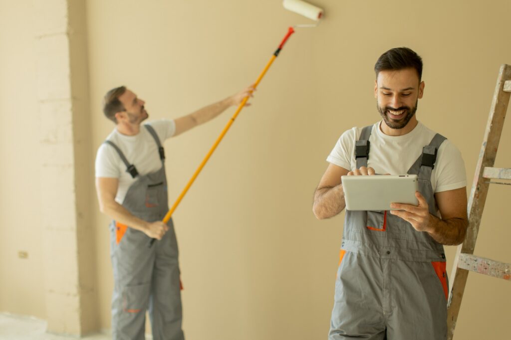 Painting contractor using AI tools on a tablet while a crew member paints a wall