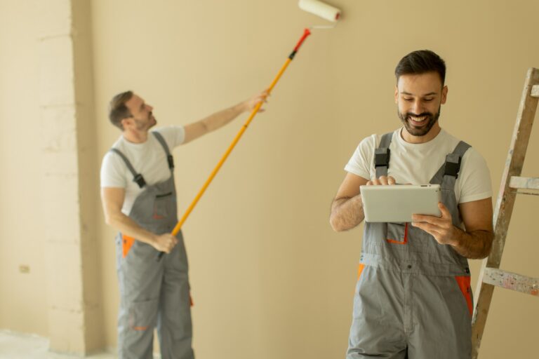 Painting contractor using AI tools on a tablet while a crew member paints a wall